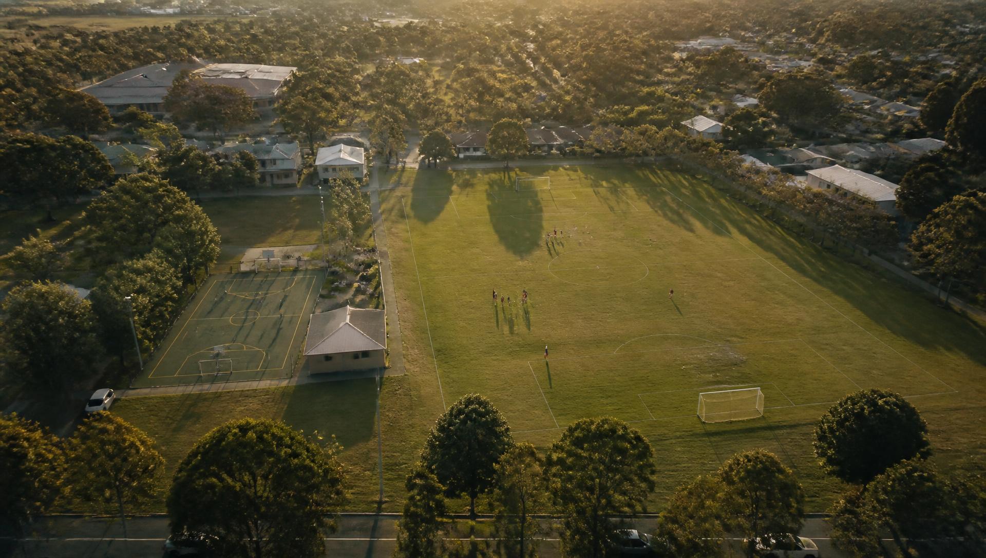 Aerial view of a community sports ground with a pitch and a court at golden hour